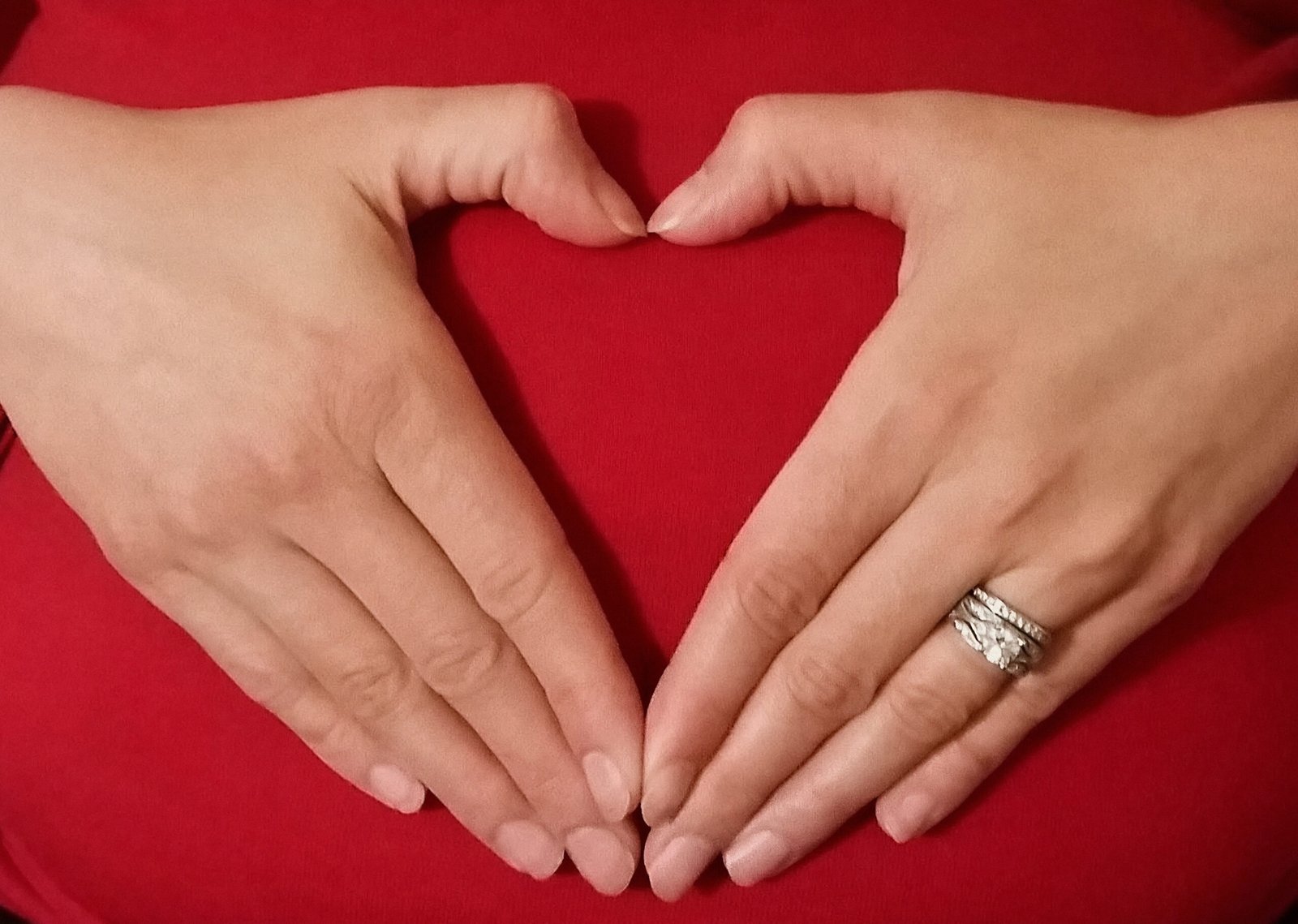 Expecting parent forming a heart with both hands over her belly